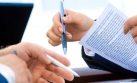 Two professionals shaking hands over papers, symbolizing contract management strategic mastery.