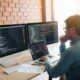a man at a desk with dual computer screens, engaged in developing a chatbot using Python programming