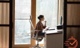 A woman at an ergonomic home office desk, focused, with a window view brightening her workspace.