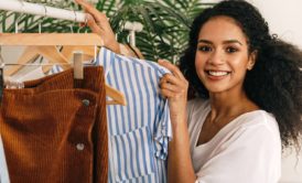 A woman happily holding a shirt on a rack, showcasing trendy fashion styles for ladies