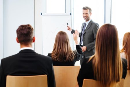 A professional man in a suit presenting to a group of people during scrum master training