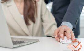 A man holding a woman's hand at a desk, highlighting a workplace affected by sexual harassment.