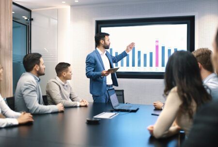 A man in formal attire presents to a group, highlighting the various types of meetings in a business context.