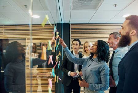 team members examining sticky notes on a glass wall as part of a user stories course activity