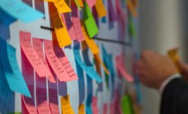 a man in a suit examines a wall covered with colorful post-it notes, reflecting agile scrum user story planning