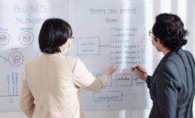 Two individuals discussing e-learning roadmap planning in front of a whiteboard filled with notes and diagrams.