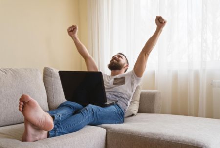 a man relaxes on a couch with his feet up, working on a laptop while exploring how to get jobs on upwork